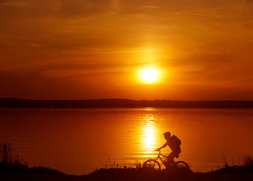 Image of sporty one tourist man walking along the shore with the bike against sunset sky with clouds and sun rays. alone woman. Silhouette race with high speed
