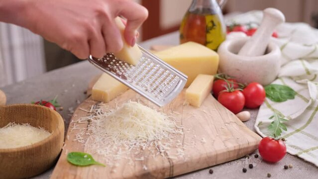 woman grates piece of parmesan hard cheese on a grater at domestic kitchen