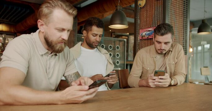 Three friends in a cafe bar using phone. Looking at smartphones unconscious about the surroundings. Three men using their smartphones while sitting in pub after work.