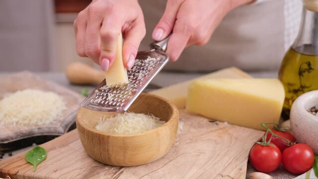woman grates piece of parmesan hard cheese on a grater at domestic kitchen