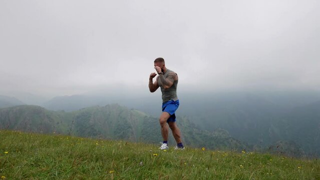 Athletic man is training and fighting in nature, handsome sporty man is boxing alone at top of mount