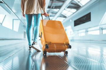 Young female traveler walking with a yellow suitcase at the modern Airport Terminal, Back view of...