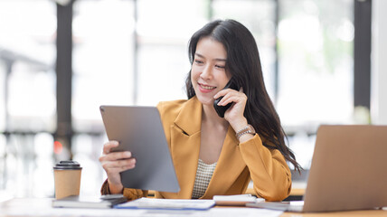 Asian Businesswoman using tablet notes while making phone call working laptop computer at workplease, Financial, accounting, report, tax, Business concept