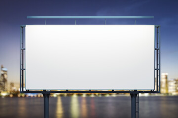 Obraz premium Blank white billboard on city buildings background at night, front view. Mockup, advertising concept