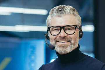 Portrait of a gray-haired handsome man in glasses and a headset with a microphone. Speaker,...