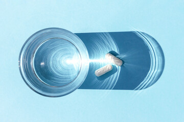 Two white pills and glass of water on blue background. Medicine, healthcare concept. Top view Flat lay