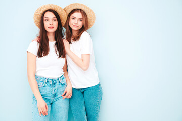 Two young beautiful smiling hipster female in trendy same summer white t-shirt and jeans clothes. carefree women posing near blue wall in studio. Cheerful and positive models in hats