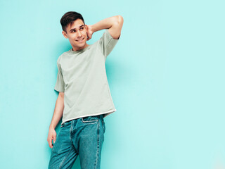 Portrait of handsome smiling stylish hipster lambersexual model.Man dressed in T-shirt and jeans. Fashion male isolated in studio. Posing near blue wall. Cheerful and happy