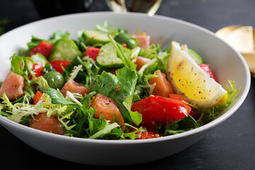 Ketogenic salad with salted salmon fish, lemon, cucumber, olives, tomatoes, green lettuce salad and honey mustard dressing. Healthy food trend.