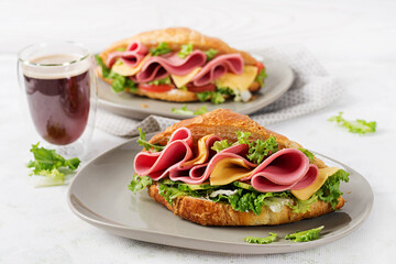 Fresh croissant or sandwich with salad, ham and cheese on light  background.