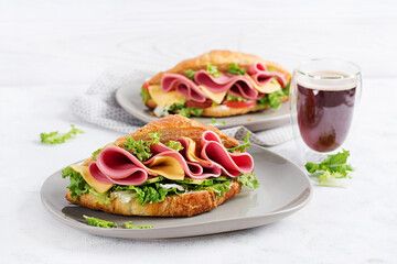 Fresh croissant or sandwich with salad, ham and cheese on light  background.
