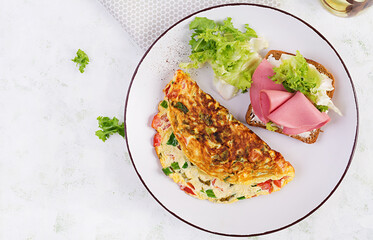 Omelette with tomatoes, cheese, green onion and sandwich with ham on white plate.  Frittata - italian omelet. Top view