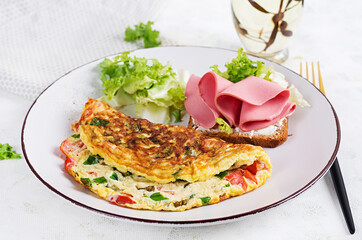 Omelette with tomatoes, cheese, green onion and sandwich with ham on white plate.  Frittata - italian omelet.