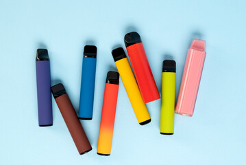 Layout of colorful disposable electronic cigarettes with shadows on a blue background. The concept of modern smoking, vaping and nicotine. Top view