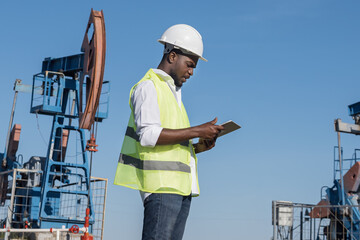 African American engineer enters information into tablet about production of crude oil standing...