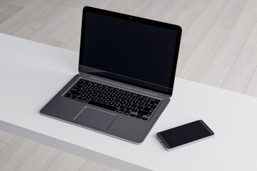 Close up of empty laptop and smartphone on light desktop, mock up place on screen, wooden parquet flooring background. Top view. 3D Rendering.