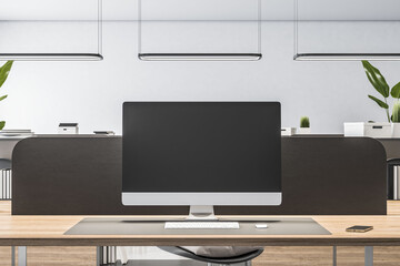 Front view on blank black monitor screen with place for your logo or text on wooden workspace table in minimalistic style office with black partition on light wall background. 3D rendering, mock up