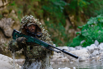 A military man or airsoft player in a camouflage suit sneaking the river and aims from a sniper...