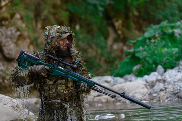 A military man or airsoft player in a camouflage suit sneaking the river and aims from a sniper...