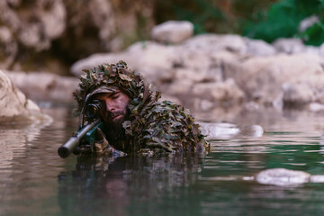 A military man or airsoft player in a camouflage suit sneaking the river and aims from a sniper...