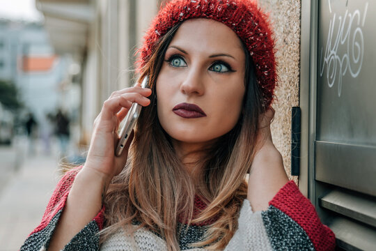 young woman with hat and winter sweater in the street talking with mobile phone
