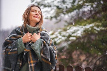Young adult relaxed woman standing in a sweater and wrapping herself in a scarf standing enjoing...