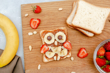 Funny owl face sandwich toast bread with peanut butter, banana, strawberry on wooden board. Cute kids childrens baby's sweet dessert, healthy breakfast,lunch, food art on gray background,top view