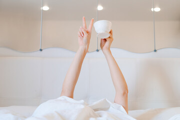 Young woman with a coffee mug in bed with white linens. Minimal happy morning morning concept.