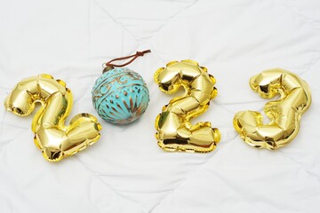 the inscription 2022 consists of inflatable golden numbers and a Christmas tree toy on a white...