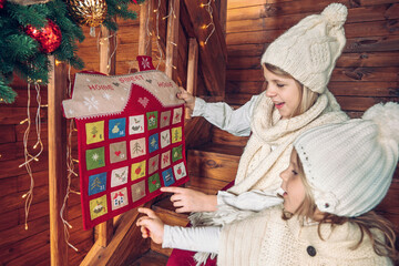 Sisters holding Christmas handmade advent calendar in a house shape