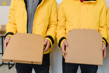 Two couriers holding cardboard pizza boxes. Brown box for shipping and delivery. Food order service and delivering concept. Fast food orders from customer at home. Place for text and advertising.