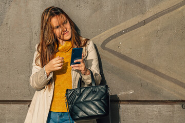 young woman with raincoat and mobile phone leaning on the wall