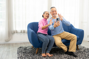 Happy smiling asian senior couple sitting on sofa and using smartphone for online video call at home living room. Smiling mature Video Call Conference talk chat online concept.