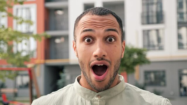 Amazed african american man shocked, saying WOW outdoor. Handsome guy wearing casual clothes surprised to camera on urban background. Male dark skinned person demonstrating surprised face expression.