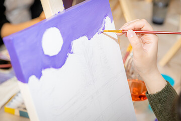 Female hand painting purple sky on a canvas during painting workshop  