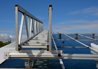 Naklejka premium aluminum footbridge for washing windows above the skylight. simplifying the washing of large greenhouses and galleries with ceiling windows. the ladder can be moved over the rails, blue sky, trowel