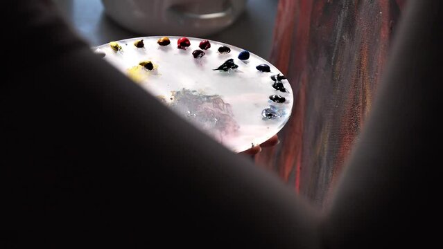 female artist  with brush mixes paint in palette while drawing picture in art studio close-up
Coloring the color compatibility for the artist
the artist works near the window in the backlight