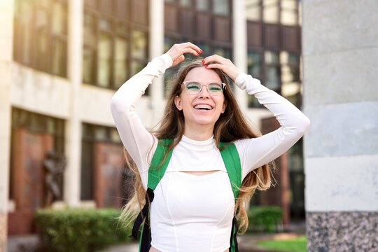 portrait of happy cheerful positive young college or university girl, young joyful beautiful woman teenager having fun outdoors at campus in glasses with backpack. Education, studying concept