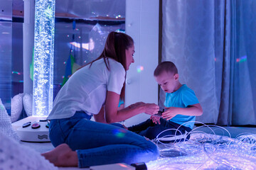 Special needs child in sensory stimulating room, snoezelen. Autistic child interacting with therapist during therapy session. - obrazy, fototapety, plakaty