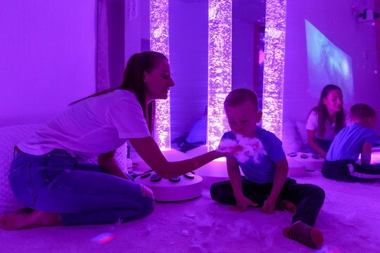 Child and therapist in sensory stimulating room, snoezelen. Autistic child  interacting with colored lights during therapy session. Stock Photo