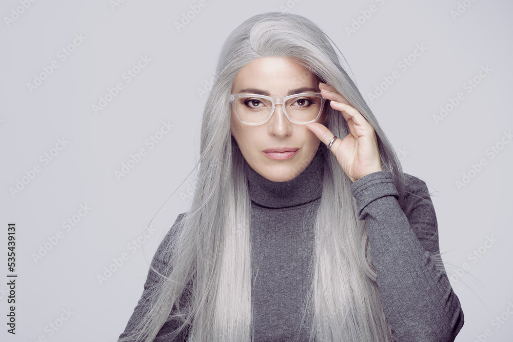 Wall mural successful business woman with long silver hair, wearing fashionable clear eyeglasses staring at cam