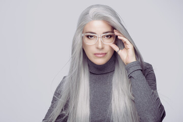 successful business woman with long silver hair, wearing fashionable clear eyeglasses staring at...
