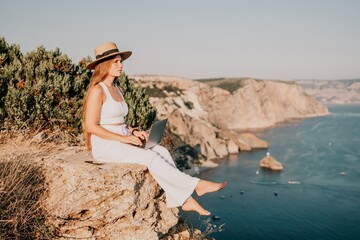 Digital nomad, Business woman working on laptop by the sea. Pretty lady typing on computer by the sea at sunset, makes a business transaction online from a distance. Freelance, remote work on vacation