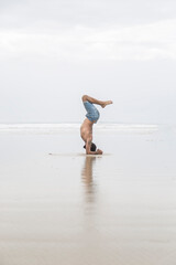 Caucasian man doing yoga poses on the sand by the sea.