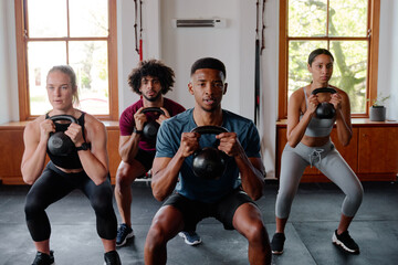 Fototapeta na wymiar Group of focused young adults doing kettlebell squats at the gym