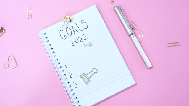 The inscription goals 2023 on notepad on pink background, top view.