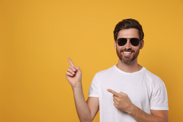 Portrait of smiling bearded man with stylish sunglasses on orange background. Space for text