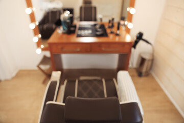 Blurred view of stylish hairdresser's workplace with armchair and professional tools in barbershop