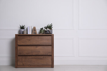 Books and beautiful plants on wooden chest of drawers near white wall indoors