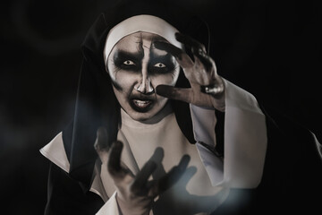 Portrait of scary devilish nun and smoke on black background. Halloween party look